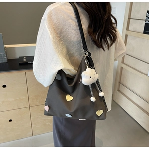 Detail of taupe tote bag with heart patches and white cloud plush charm on a model