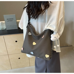 Brown tote bag with colorful heart patches and a white cloud plush charm on a model
