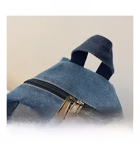Detail of dark blue denim backpack featuring YKK bronze dual zippers and webbing handle