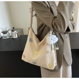 Detail of canvas tote bag featuring heart leather patches and white cloud plush charm