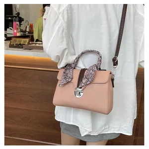 Detail view of pink textured leather crossbody bag with decorative silk scarf on handle