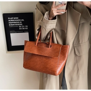 Detail of caramel brown croc-embossed tote bag with flap closure held by a model