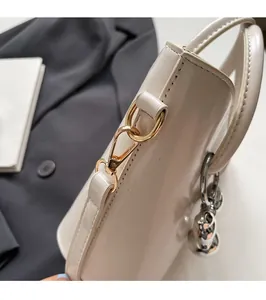 Close-up of golden metal clasp and silver pendant on cream glossy leather bucket bag