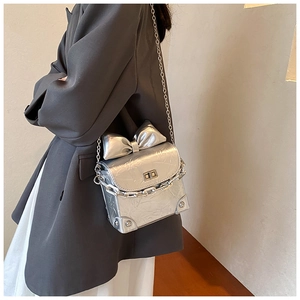 Detail of silver metallic mini bag with bow accent and chain strap worn by model