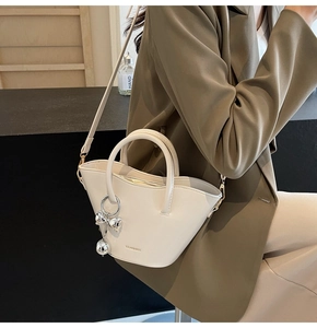 Detail of cream leather bucket bag featuring a silver bow charm and branded logo