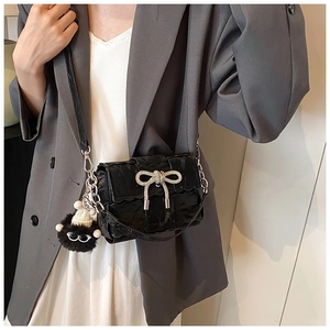 Détail du sac en cuir verni noir avec un nœud étincelant et un porte-clé en peluche