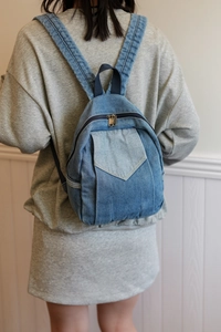 Mini blue denim backpack with front pocket shown on model in a casual lifestyle setting