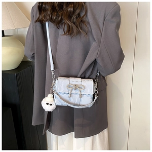 Détail du sac bandoulière bleu clair tissé avec nœud en strass et breloque peluche