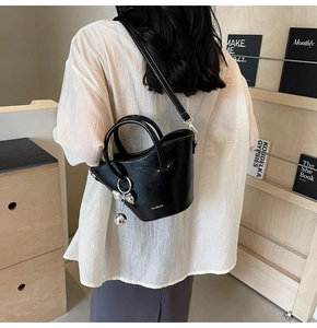 Detail of black leather bucket bag with silver charm and brand logo held by a model