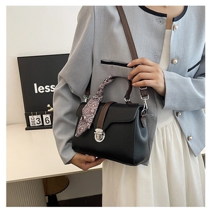 Detail of black pebbled leather handbag with silk scarf handle and silver twist lock