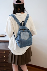 Detail of blue denim mini backpack showing washed texture and flap pocket on back