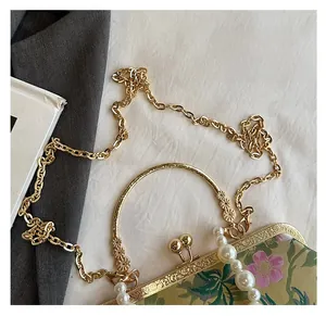 Detail of floral embroidery bag with large pearl handle and golden chain strap