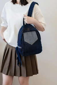 Detail of dark blue denim mini backpack showing contrast pocket and adjustable straps