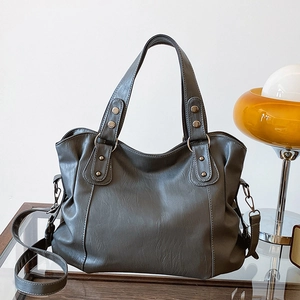 Minimalist charcoal grey PU leather tote bag with dual handles and metal rivets on a table