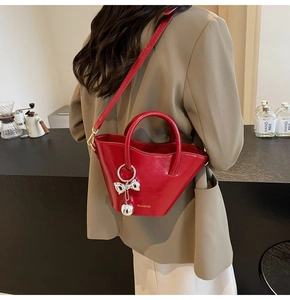 Detail view of a red leather bucket bag featuring a silver bow charm and shoulder strap