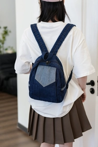 Rear view of a model wearing the small dark blue denim backpack with light blue pocket