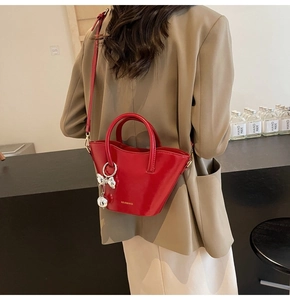Detail of red bucket bag with silver bow charm and crossbody strap on a black counter