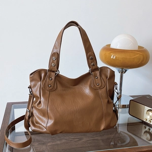 Brown vintage faux leather tote bag with metal rivets and adjustable strap in cozy setting