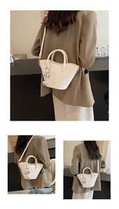 Detail of cream bucket bag with silver ball and bow charms worn on a crossbody strap
