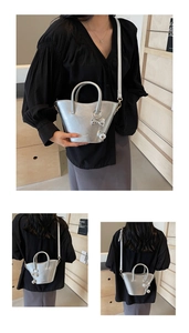 Detail view of silver metallic bucket bag with metal bow charm and round handle