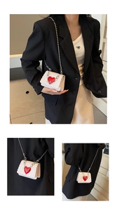 Detail of white mini crossbody bag with heart motif, wavy edges and silver ball chain strap