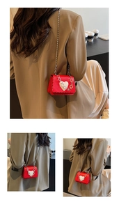 Detail of red mini shoulder bag with wave edge and silver ball chain strap on a model