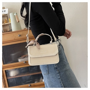 Close-up of beige woven crossbody bag with silk scarf handle and leather trim details