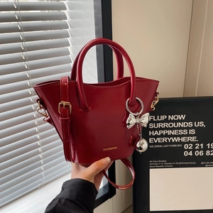 Glossy burgundy bucket handbag with adjustable strap and metal bow charm in 2024 style