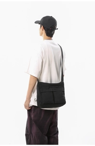 Detail view of black canvas crossbody bag with large double pockets on male model back