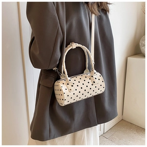 Detailed side view of a white polka dot Boston barrel bag worn on a woman's shoulder