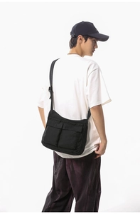 Close-up of black canvas messenger bag featuring large utility flap pockets and wide strap