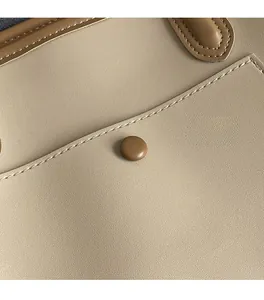 Detail of beige textured fabric with brown leather trim and decorative snap button