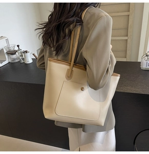 Detail of a large beige tote bag with brown trim and shoulder strap on a female model