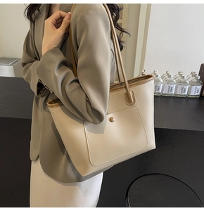 Detail of a large beige tote bag with brown trim and front snap pocket for daily commute
