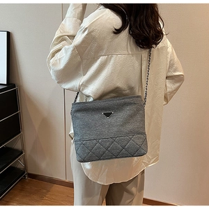 Detail of gray quilted nylon crossbody bag with metallic chain strap worn by a model