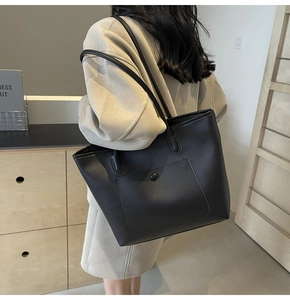 Detail of a large black leather tote bag with functional front pocket and slim shoulder straps