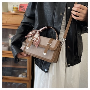 Detail of a brown leather and canvas crossbody bag with decorative scarf-wrapped handle