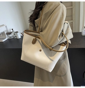 Close-up of a minimalist cream tote bag with brown contrast piping and shoulder strap