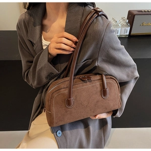 Detailed view of a brown suede bag with white stitching and leather handle on a desk