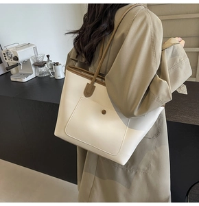 Detail of a large cream tote bag with brown straps and a round buckle front pocket