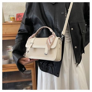 Detail of cream crossbody bag with silk scarf handle and silver hardware accent
