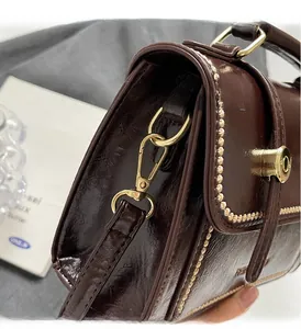 Detail of dark brown glossy leather bag with premium gold hardware and elegant stitching
