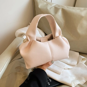 Pink minimalist dumpling bag with lychee texture and gold ring handle on a soft sofa
