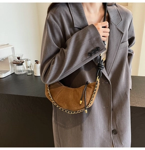 Detail of a brown suede croissant bag featuring gold chain and knotted leather strap