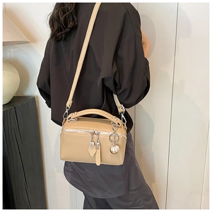 Détail du sac Boston beige avec texture litchi et pendentif boule argentée élégant