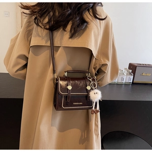 Detail view of coffee leather handbag featuring pearl rivets and a cute plush monster charm