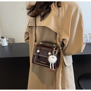 Detail of dark brown vintage crossbody bag with gold rivets and plush monster charm