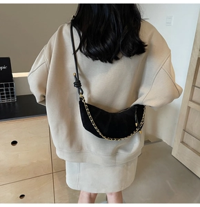 Detail of black crescent crossbody bag with gold chain and unique knotted strap detail