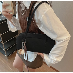 Detail of black rectangular shoulder bag with silver ring and woven ball pendant charm