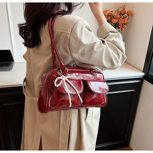 Close-up of burgundy patent leather bag featuring double pockets and pearl bow charm